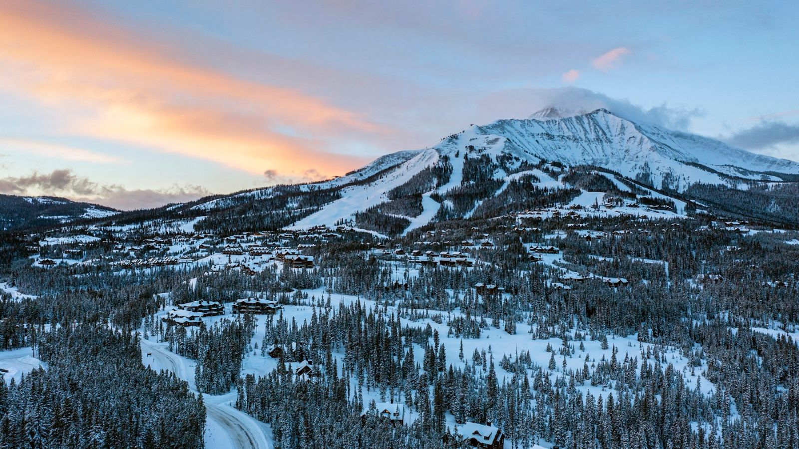Lone Peak above snow-covered homes and forest in Big Sky, Montana, at sunrise